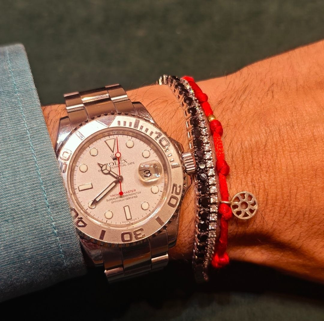 Pulseira Kaballah de fio vermelho no pulso, usada ao lado de relógio e bracelete de brilhantes